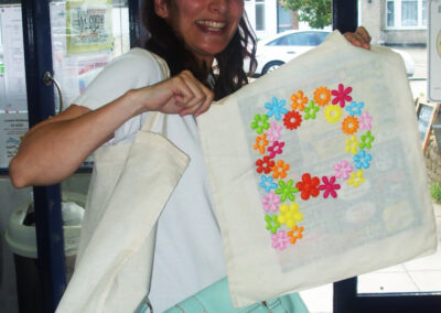 Woman smiling, holding decorated tote bag with a floral "P," bag decorating project.