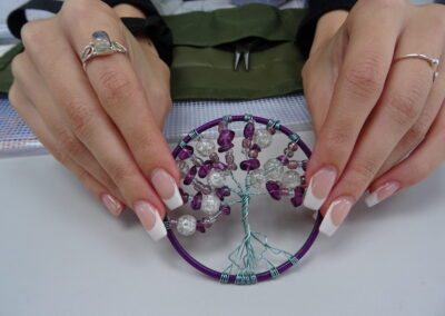 Hands holding a wire tree of life pendant with purple and clear beads.