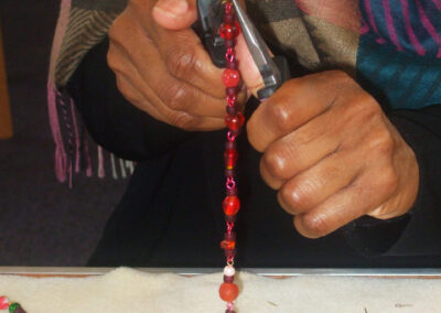 Hands creating red beaded jewellery with pliers.