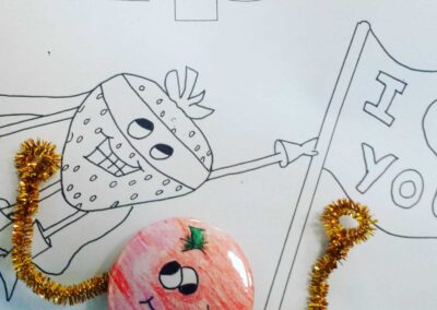 Cute fruit superhero art: Strawberry with mask and apple button with pipe cleaner arms. "I ❤️ You" flag.