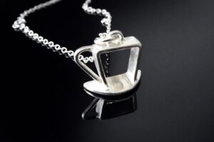 Silver coffee cup pendant necklace on a black reflective surface.