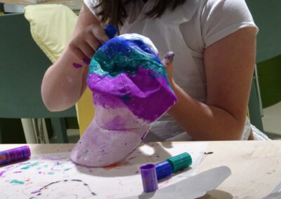 Person painting a colorful baseball cap with purple, white, and teal paint.