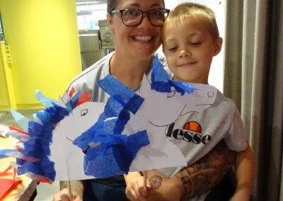 Woman and child holding handmade paper horse puppet with blue and red decorations.