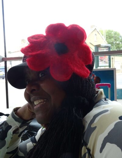 Smiling woman in hat with large red flower, wearing camouflage jacket.