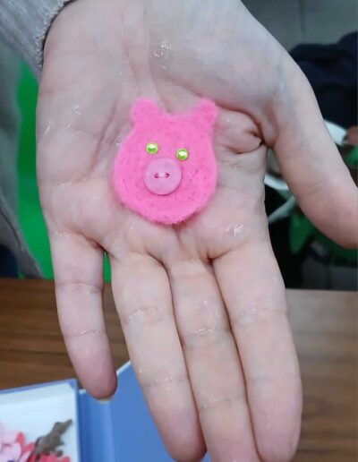 Hand holding a handmade pink felt pig with button nose and green eyes.