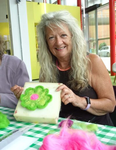 Woman showing felt flower craft on foam. Colorful wool fibers on table.