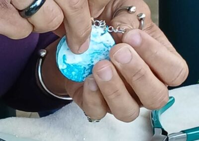Hands assembling a blue and white resin pendant necklace.