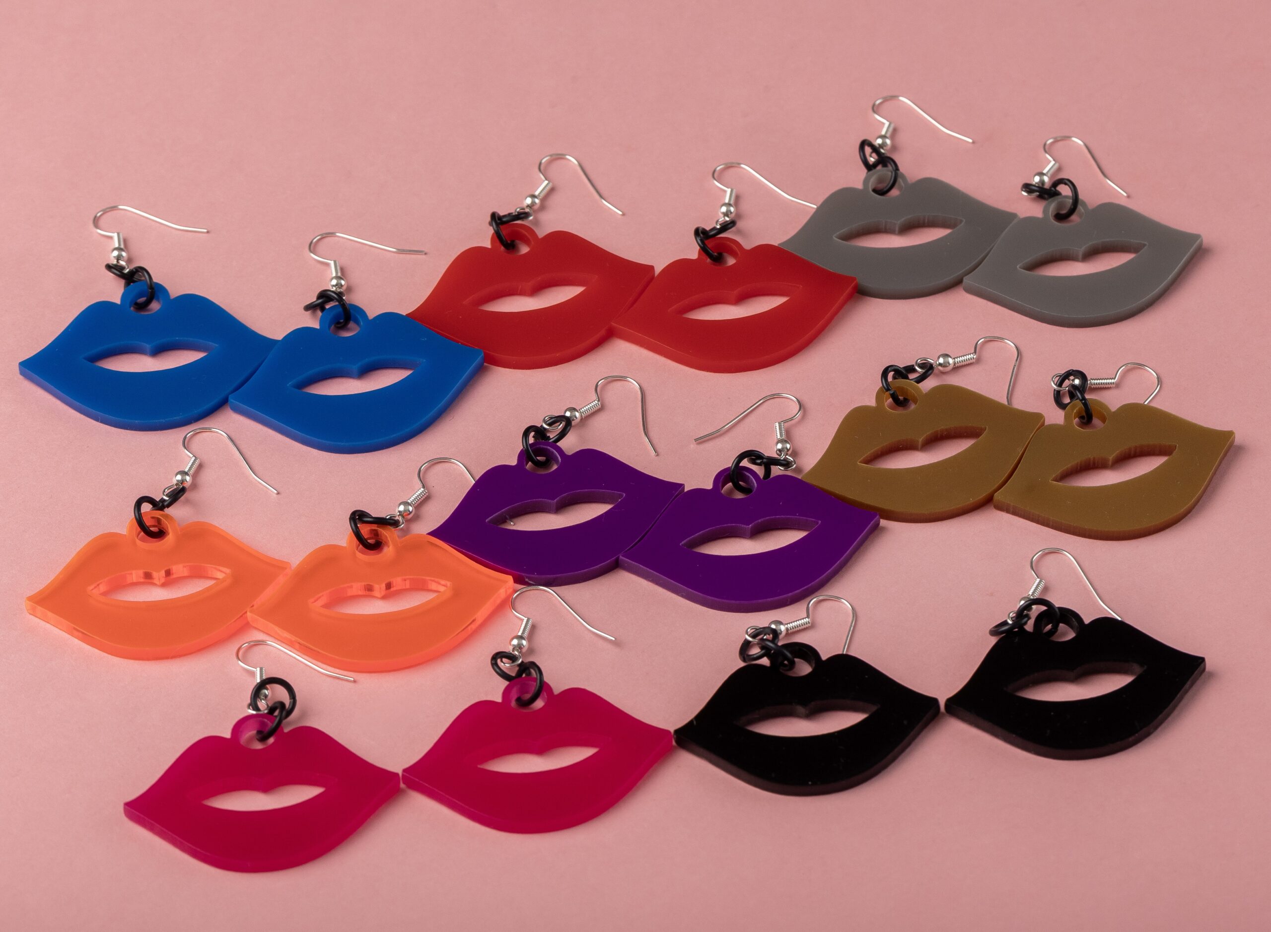 Colorful lip-shaped earrings in various colors on a pink background