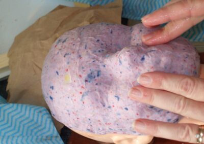 Hands shaping paper pulp bowl; colorful recycled paper craft.
