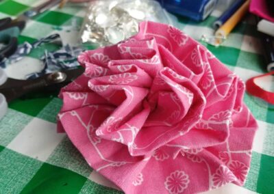 Pink fabric flower on a green and white checkered table with crafting supplies.