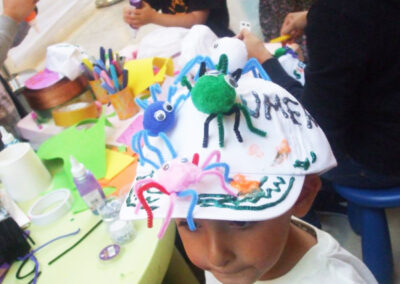 Child wearing a decorated spider hat at a craft table with other kids.