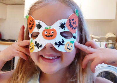 Girl wearing a Halloween mask decorated with pumpkins and spiders, smiling.