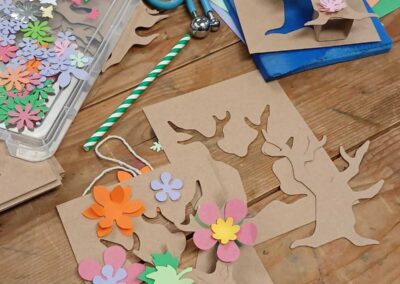 DIY spring craft project: Paper tree cutouts being decorated with colorful paper flowers and leaves.