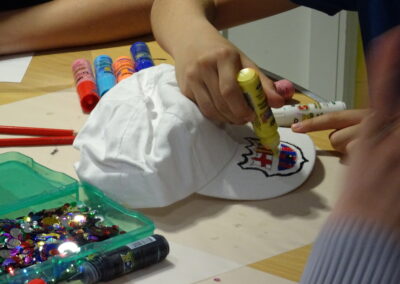 Decorating a white baseball cap with colorful paint pens and sequins.